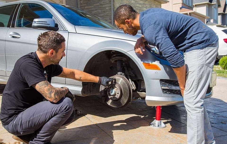 Dos técnicos trabajando en el freno de un automóvil durante un servicio de reparación de automóviles móvil.